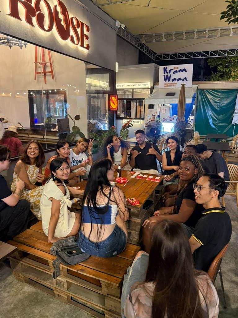 Group of people seated around a wooden table at an outdoor cafe in the evening
