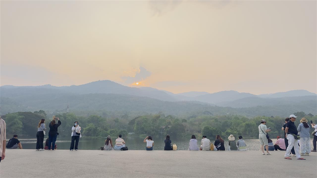 People watching the sunset over a lake and hazy mountains