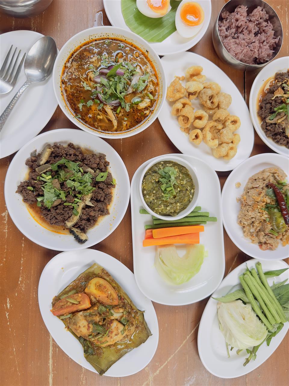 Northern Thai dishes on a wooden table, including chilli dip, soup and sticky rice