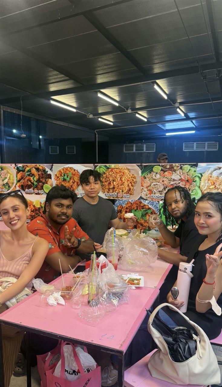 Group sharing Thai street food at a pink table in front of menu boards